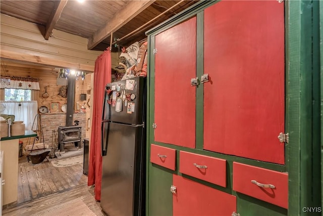 kitchen with freestanding refrigerator, wood finished floors, a wood stove, wooden ceiling with exposed beams, and green cabinets