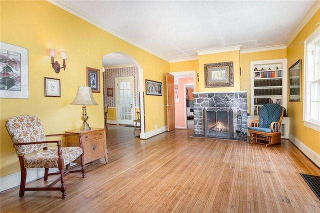 sitting room with arched walkways, a fireplace, wood finished floors, ornamental molding, and baseboards