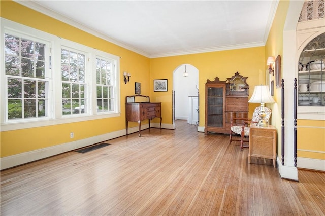 sitting room with light wood-style flooring, ornamental molding, baseboards, and arched walkways