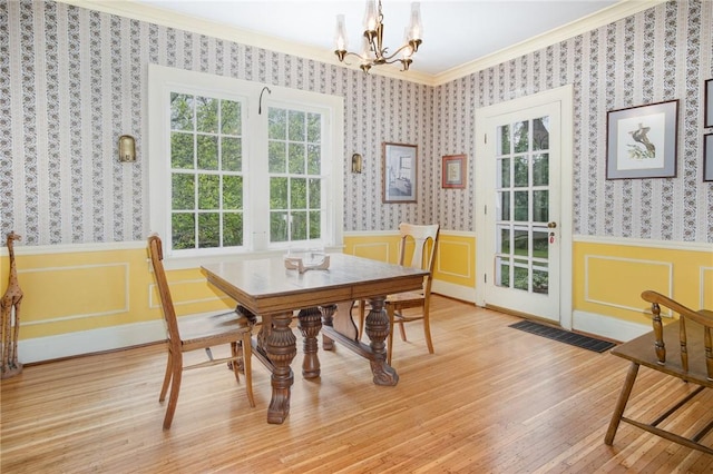 dining area with ornamental molding, a chandelier, wainscoting, light wood-style flooring, and wallpapered walls