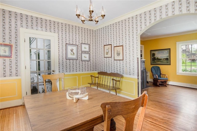 dining space with ornamental molding, arched walkways, a chandelier, wood finished floors, and a wainscoted wall