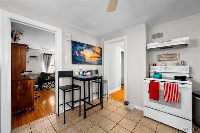 kitchen featuring white range with electric cooktop, under cabinet range hood, light tile patterned floors, a ceiling fan, and baseboards