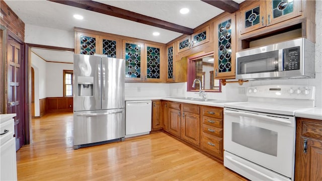kitchen featuring appliances with stainless steel finishes, a sink, light wood-type flooring, beam ceiling, and brown cabinetry