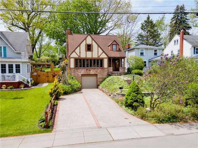 tudor home featuring stone siding, driveway, a chimney, an attached garage, and a front lawn