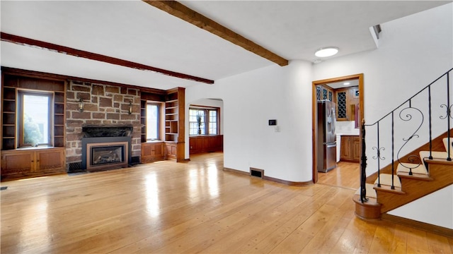 unfurnished living room with beam ceiling, baseboards, a stone fireplace, light wood-type flooring, and arched walkways