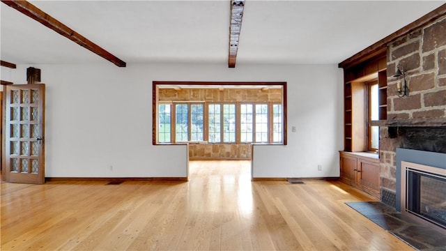 unfurnished living room featuring baseboards, a large fireplace, beamed ceiling, light wood finished floors, and built in shelves