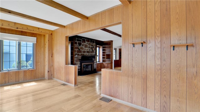 unfurnished living room featuring wood walls, beamed ceiling, wood finished floors, a stone fireplace, and baseboards