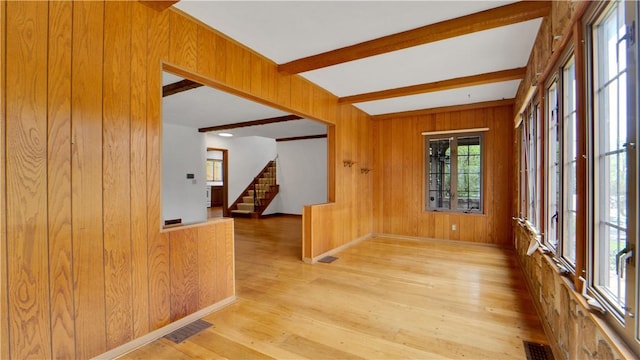 empty room with wooden walls, stairway, beam ceiling, light wood-style floors, and baseboards