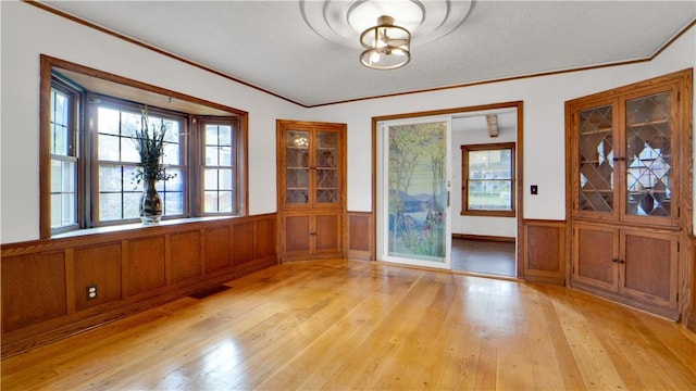 entryway with light wood-style floors, a wainscoted wall, and ornamental molding