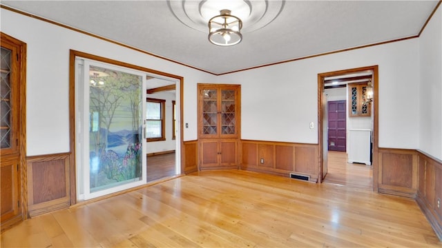 unfurnished dining area featuring ornamental molding, a wainscoted wall, and light wood finished floors