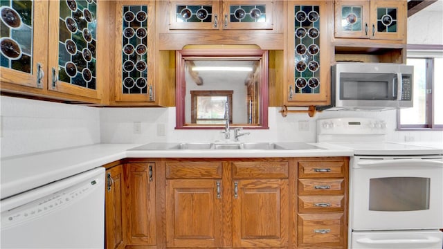 kitchen featuring white appliances, glass insert cabinets, brown cabinetry, and light countertops