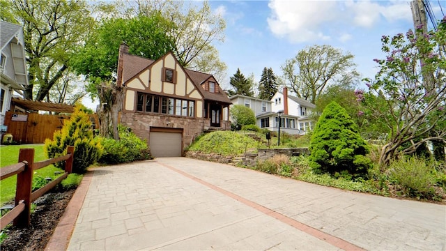 tudor house featuring stone siding, driveway, an attached garage, a chimney, and stucco siding
