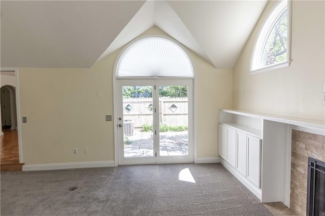 unfurnished living room featuring lofted ceiling, carpet floors, a fireplace, arched walkways, and baseboards