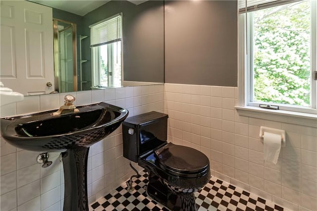 bathroom featuring tile walls, plenty of natural light, a wainscoted wall, a sink, and toilet