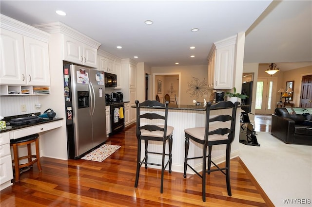 5067 William St, Lancaster, NY 14086 - kitchen featuring black appliances, a breakfast bar, white cabinetry, dark wood-type flooring, and a peninsula