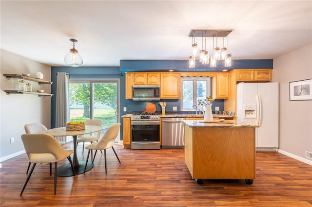 kitchen with stainless steel appliances, a kitchen island, baseboards, dark wood-type flooring, and light stone countertops