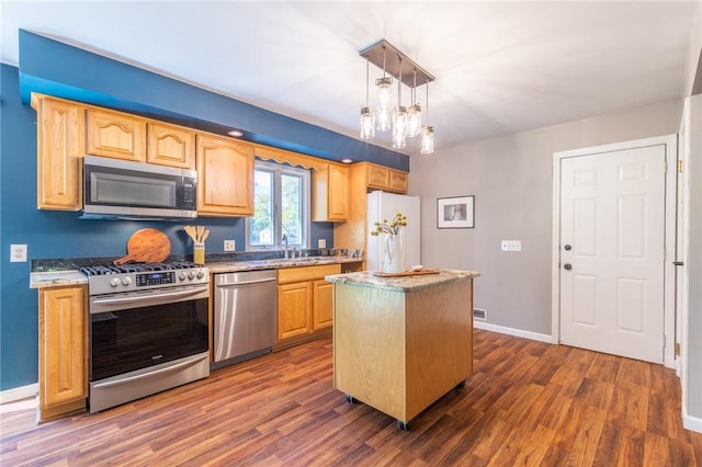 kitchen featuring appliances with stainless steel finishes, dark wood finished floors, a kitchen island, baseboards, and light brown cabinetry