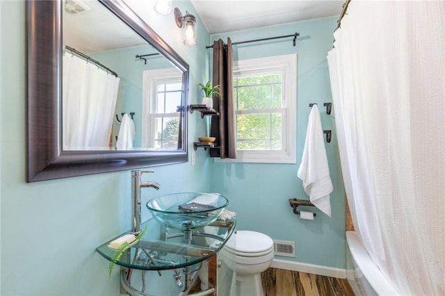 bathroom with wood finished floors, toilet, a sink, baseboards, and shower / tub combo with curtain