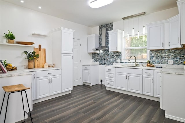kitchen featuring a sink, wall chimney range hood, white cabinets, dark wood-style floors, and tasteful backsplash
