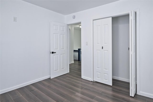 unfurnished bedroom with dark wood-style floors, baseboards, and a closet