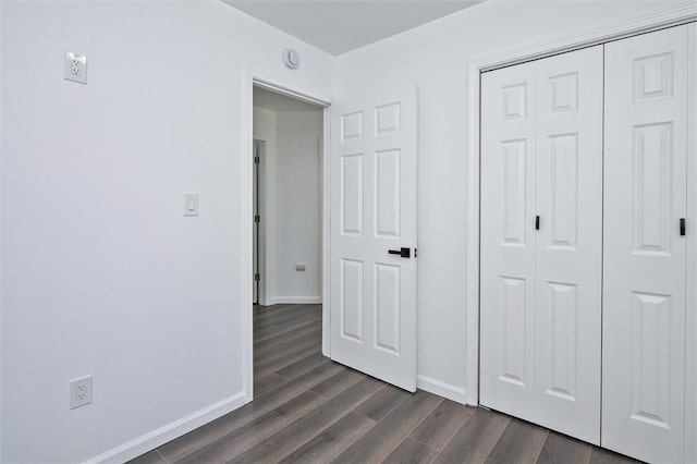 unfurnished bedroom with baseboards, dark wood-style flooring, and a closet