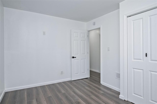 unfurnished bedroom featuring dark wood-style flooring, baseboards, and a closet