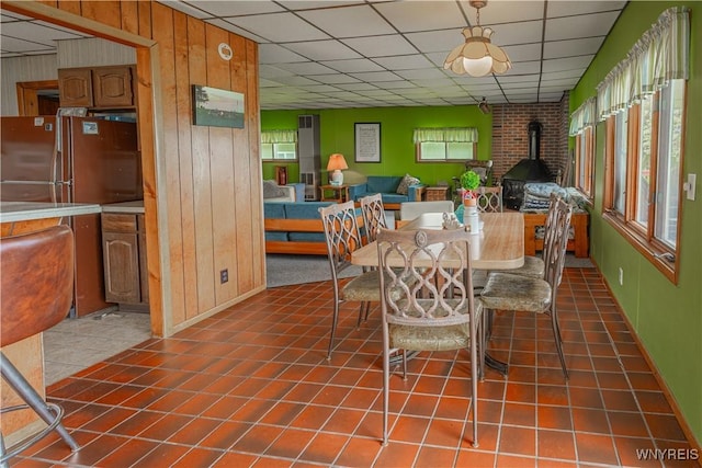 4609 E Lake Rd, Wilson, NY 14172 - dining space featuring a wood stove, healthy amount of natural light, wood walls, a paneled ceiling, and tile patterned floors