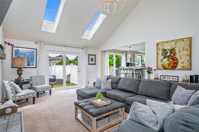 carpeted living room featuring high vaulted ceiling, a skylight, and a chandelier