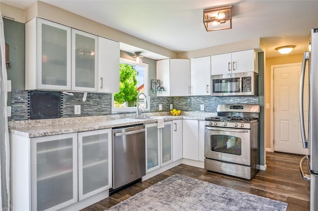 kitchen with appliances with stainless steel finishes, a sink, dark wood-style floors, white cabinets, and backsplash