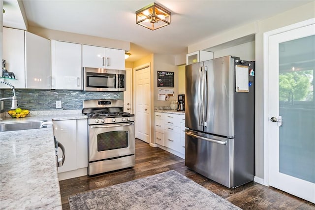 kitchen featuring appliances with stainless steel finishes, a sink, white cabinets, dark wood-style flooring, and tasteful backsplash