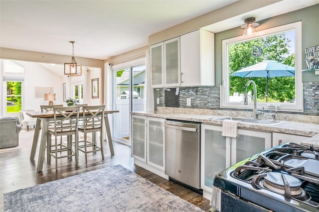 kitchen with stainless steel dishwasher, a sink, gas range oven, backsplash, and white cabinets