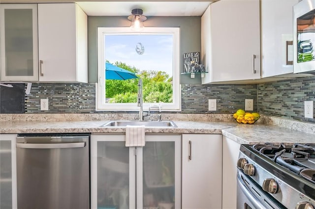 kitchen featuring appliances with stainless steel finishes, a sink, white cabinets, glass insert cabinets, and tasteful backsplash