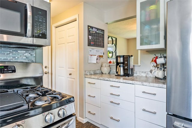 kitchen featuring appliances with stainless steel finishes, glass insert cabinets, tasteful backsplash, white cabinetry, and light stone countertops