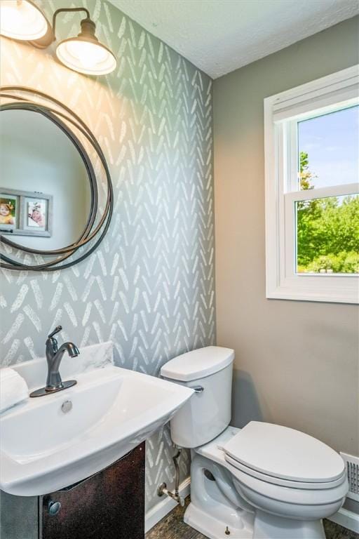 half bathroom with wallpapered walls, toilet, a sink, baseboards, and a textured ceiling