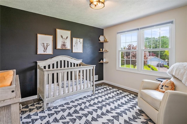 bedroom with baseboards, a nursery area, a textured ceiling, and wood finished floors