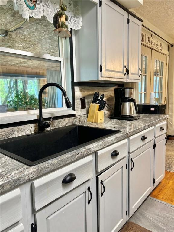 4600 College Ave, Corning, NY 14830 - kitchen featuring a sink, white cabinetry, light wood finished floors, backsplash, and a textured ceiling
