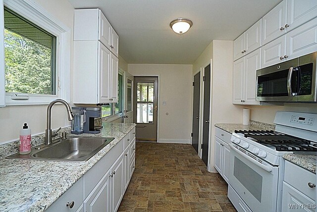 458 Kenwood Dr, Lewiston, NY 14092 - kitchen with white gas range oven, stainless steel microwave, a sink, stone finish flooring, and white cabinets