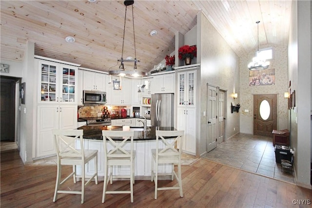 7030 Peckham Rd, Watson, NY 13367 - kitchen with stainless steel appliances, dark countertops, light wood-style flooring, a center island with sink, and white cabinets