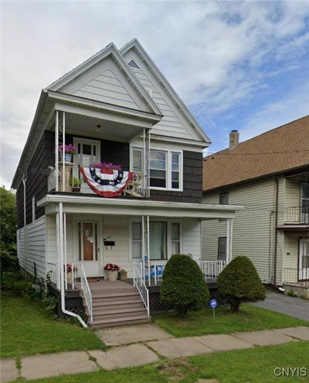 view of front of property with covered porch, a balcony, and a front lawn