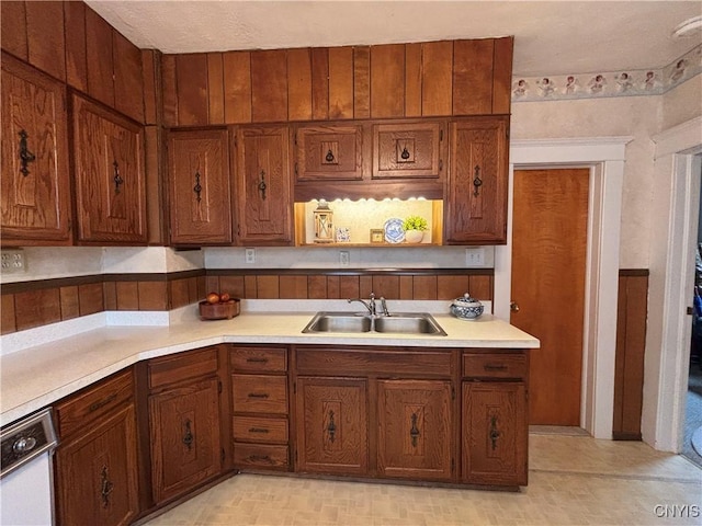 kitchen with a sink, light countertops, brown cabinetry, and white dishwasher