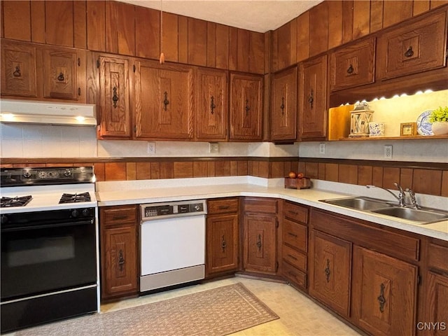 kitchen with gas range, under cabinet range hood, a sink, white dishwasher, and brown cabinets
