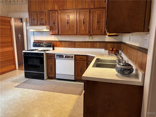 kitchen with gas range, dishwasher, a sink, under cabinet range hood, and brown cabinets