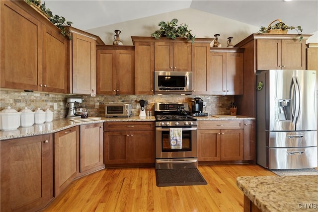 146 Edwards Falls Ln, Manlius, NY 13104 - kitchen with stainless steel appliances, vaulted ceiling, brown cabinets, light wood finished floors, and light stone countertops