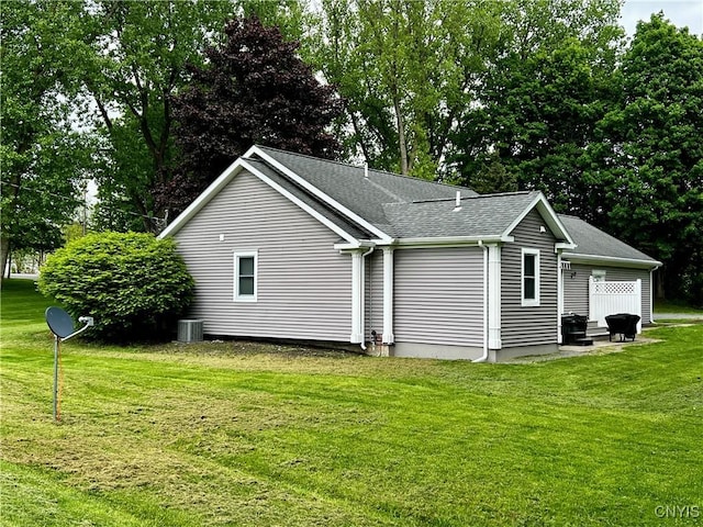 view of property exterior with central AC unit, a yard, roof with shingles, and view of wooded area