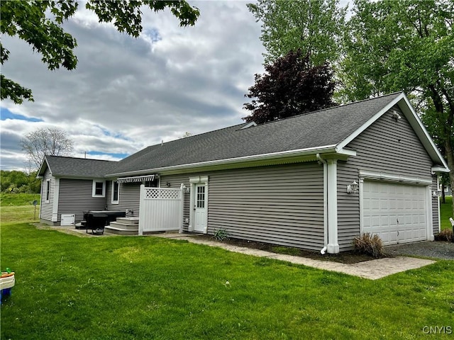 back of house with an attached garage, a lawn, and a shingled roof