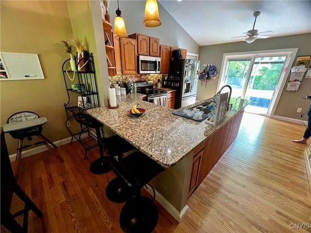 kitchen with stainless steel appliances, brown cabinetry, vaulted ceiling, light wood-style floors, and tasteful backsplash