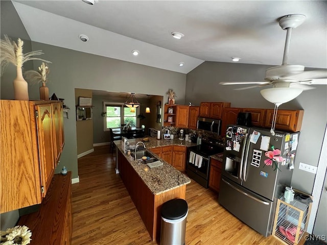 kitchen featuring appliances with stainless steel finishes, a sink, a peninsula, lofted ceiling, and light wood-style floors