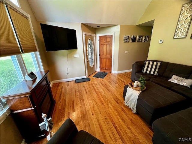 living area featuring lofted ceiling, baseboards, and light wood-style flooring