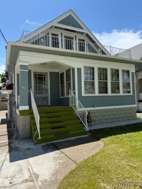 view of front of house featuring covered porch, a balcony, and a front yard