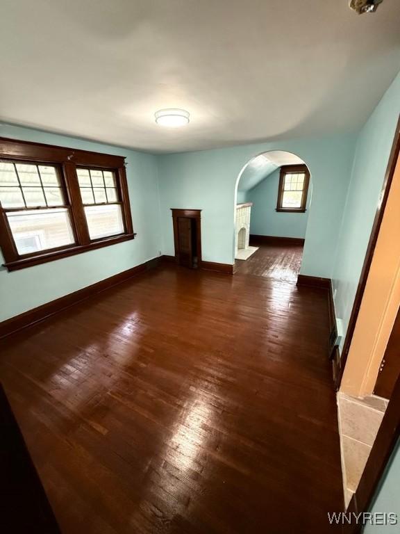 unfurnished living room with arched walkways, dark wood-style flooring, baseboards, and a fireplace